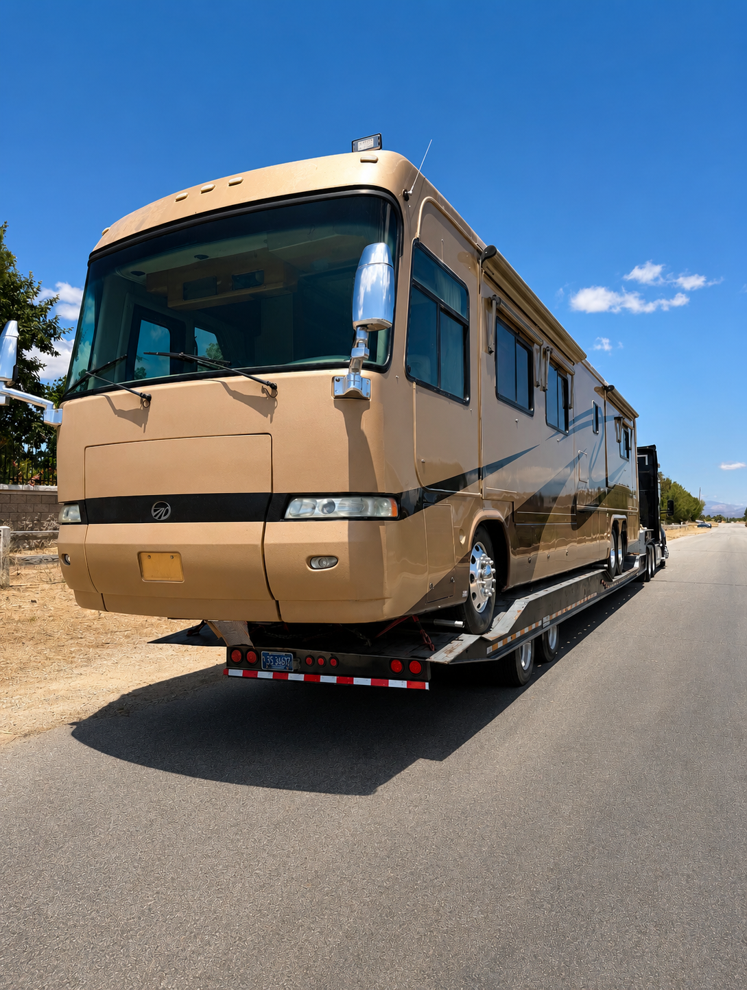 Tan luxury Monaco motorhome loaded on a Johnny's Lightning Transportation trailer, front view